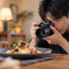 明るいレンズを付けたミラーレスカメラで料理を撮影する日本人男性