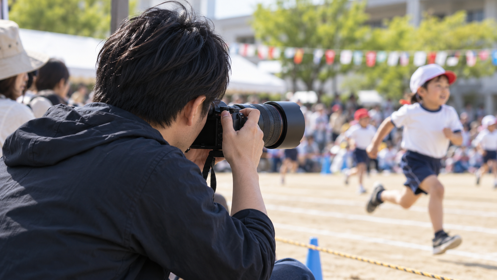 望遠レンズ付きミラーレスカメラで運動会を撮影する日本人男性