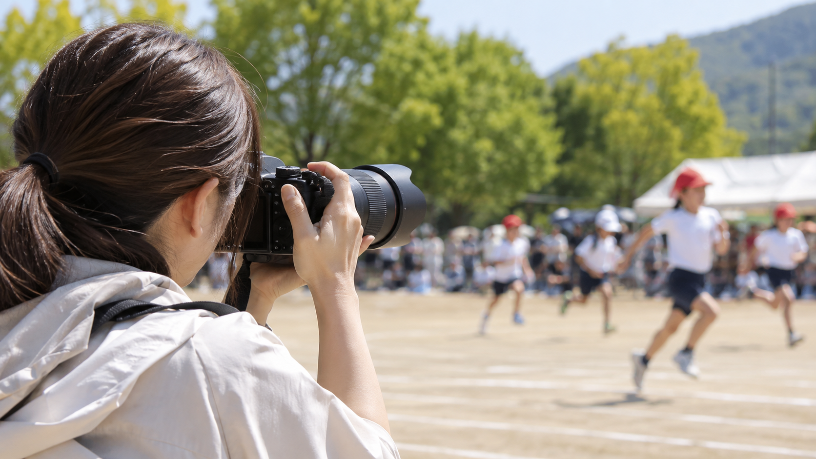 運動会で望遠ズームレンズを使って走る子どもを撮影する日本人女性