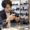 中古カメラ店でミラーレスカメラの状態を比較する日本人男性