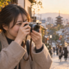 小型ミラーレスカメラで夕暮れの街を撮影する日本人女性