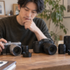 2台の中古カメラとレンズを比較しながら購入先を検討する男性