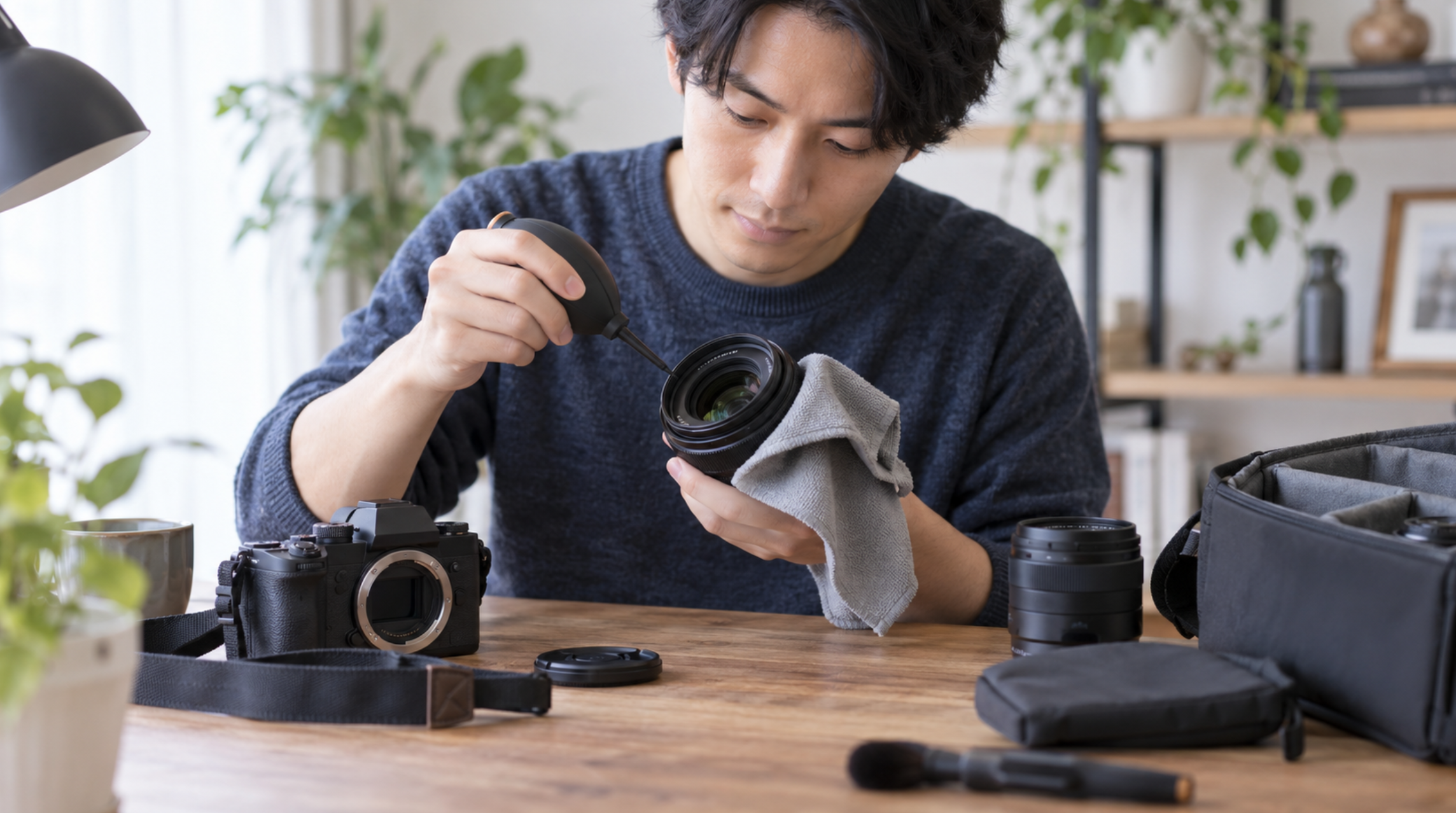 ブロアーとクリーニングクロスでカメラレンズを手入れする日本人男性