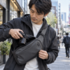 街撮りでスリングバッグからカメラを取り出す日本人男性