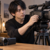 家庭用ビデオカメラと映像制作用大型カメラを比較する日本人男性