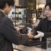 カメラ専門店の店頭でカメラとレンズを持ち込み査定する様子