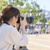 運動会で望遠レンズ付きカメラを使って子どもを撮影する家族
