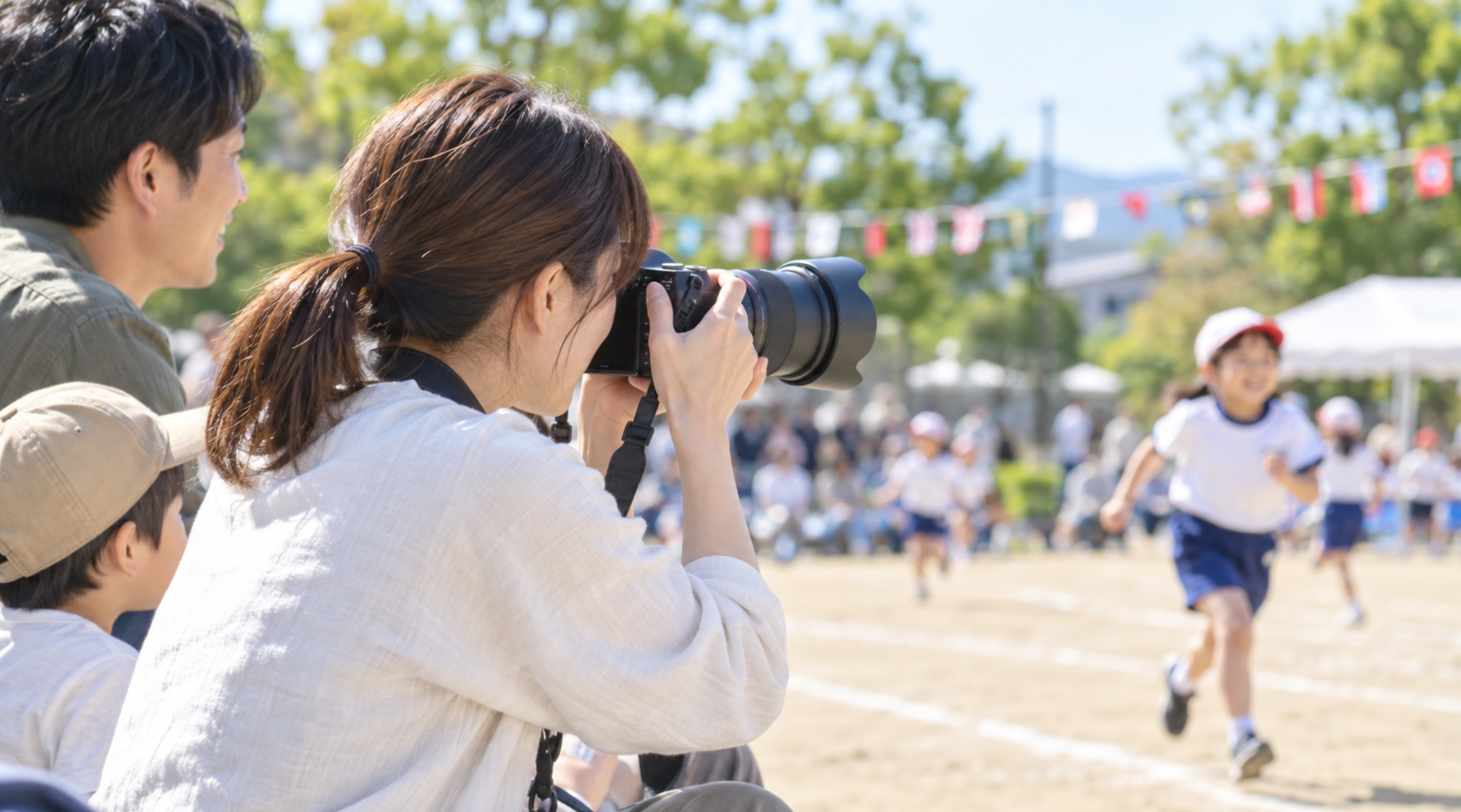 運動会で望遠レンズ付きカメラを使って子どもを撮影する家族