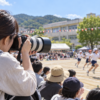 運動会で望遠レンズ付きカメラを使って子どもを撮影する日本人の保護者