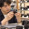 中古カメラ店で小型ズームレンズの前玉や鏡筒を確認する日本人男性