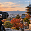 紅葉と寺院の塔が広がる夕暮れの風景を三脚に固定したミラーレスカメラで撮影する様子
